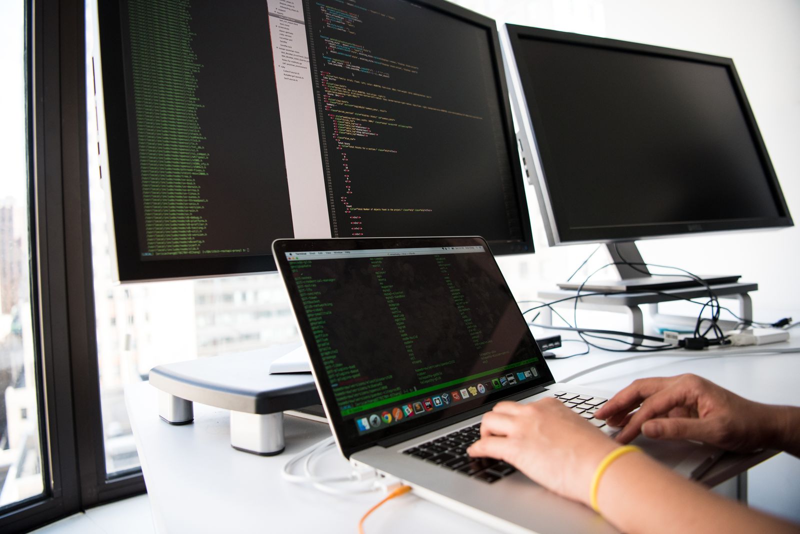 A person using a laptop at a desk with two external monitors