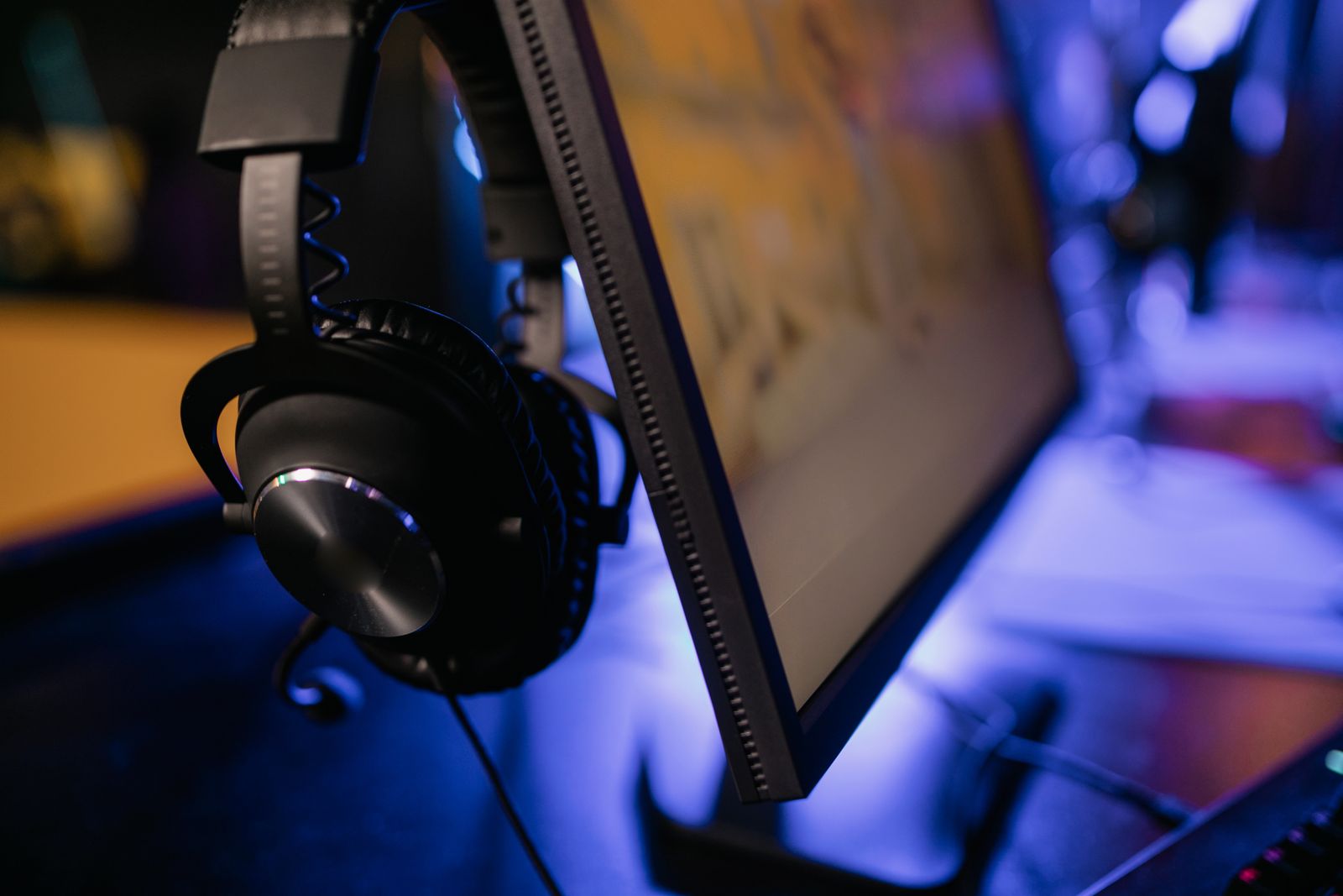 Headphones hanging beside a monitor in an illuminated gaming workspace