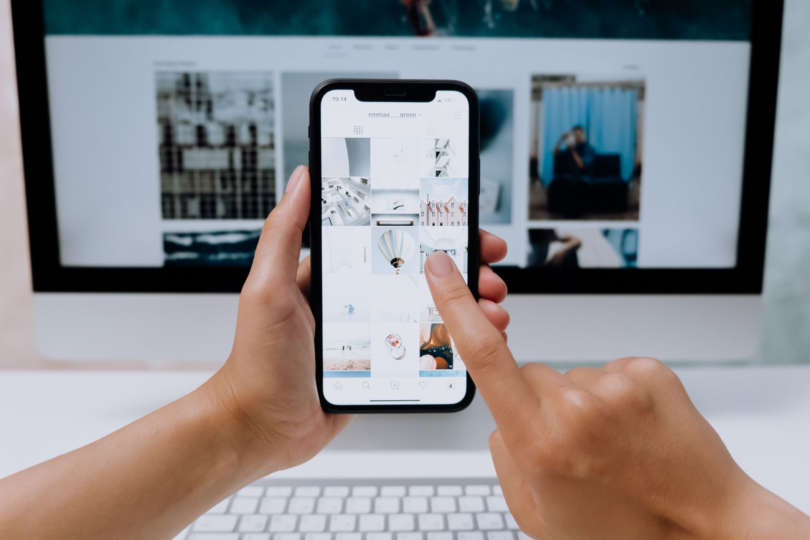 Hands using a smartphone in front of a desktop computer