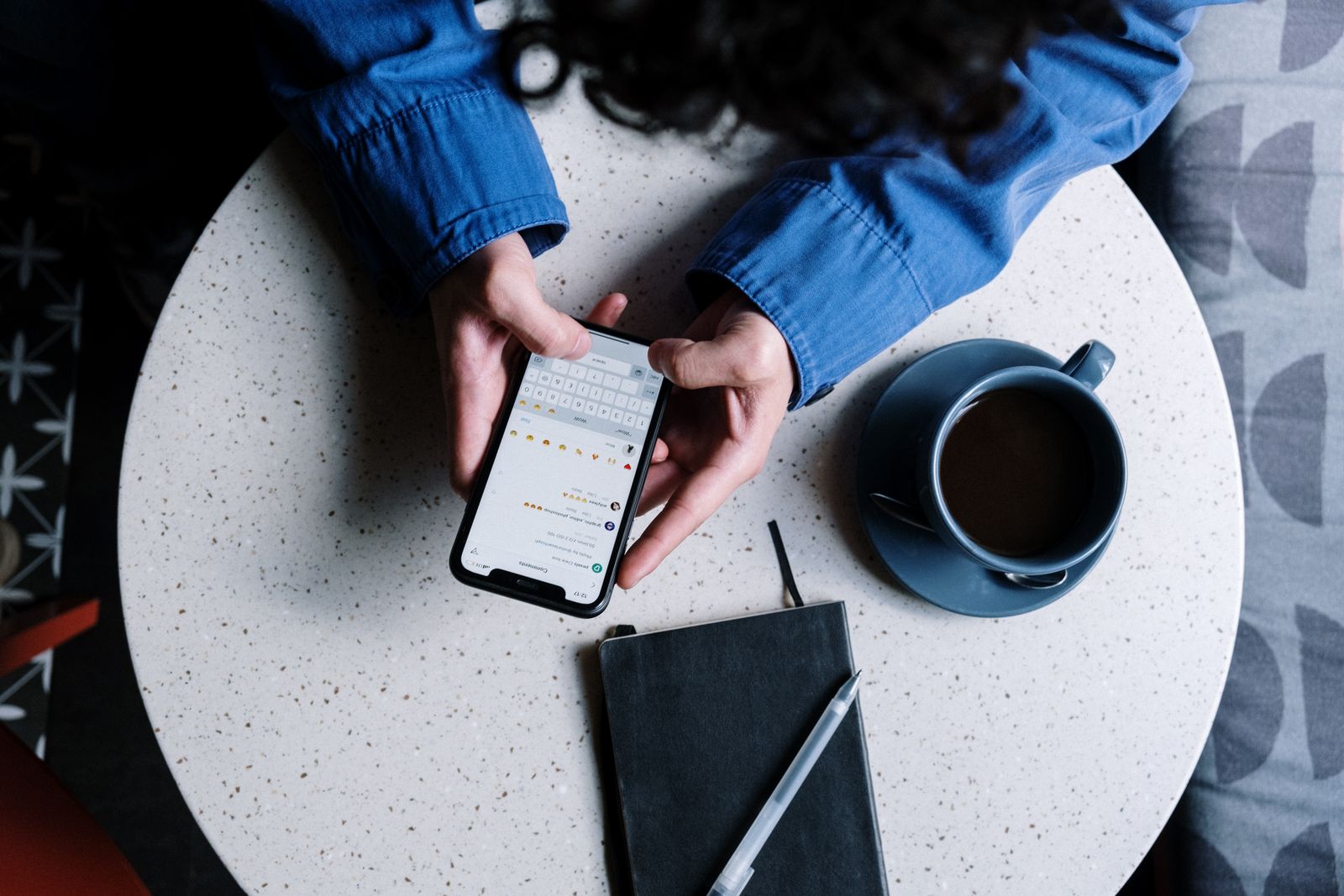 A person checking a smartphone beside a cup of coffee and notebooks